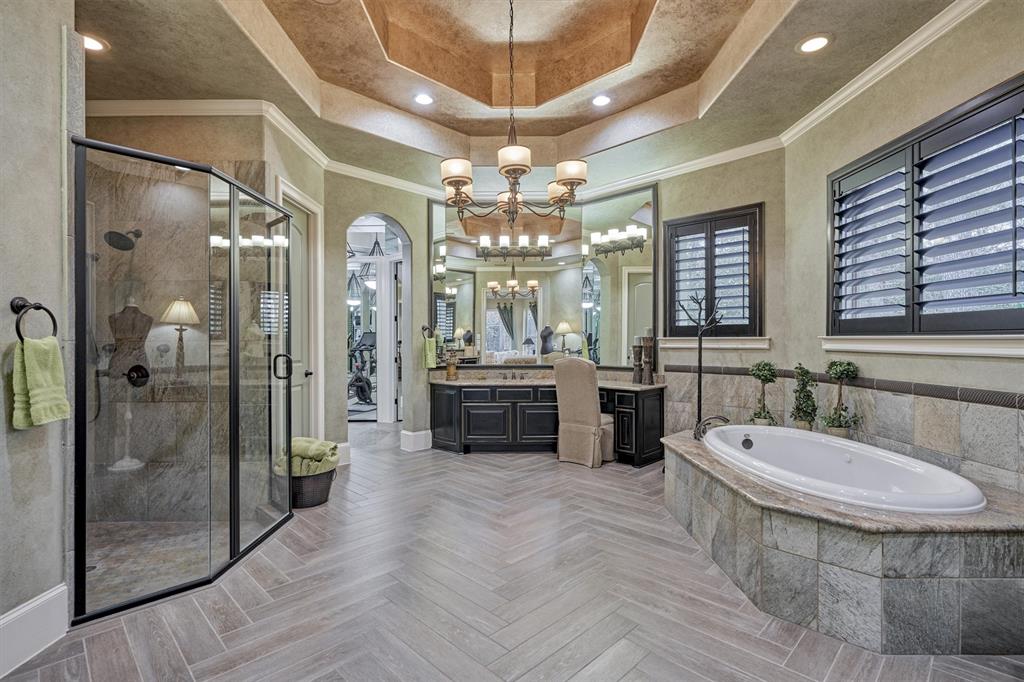 The Primary Suite Bathroom has herringbone tile floors, custom lighting, plantation shutters, jetted tub, large walk-in shower with multiple heads, dual vanities, a mirrored Dressing/Exercise area and much more.