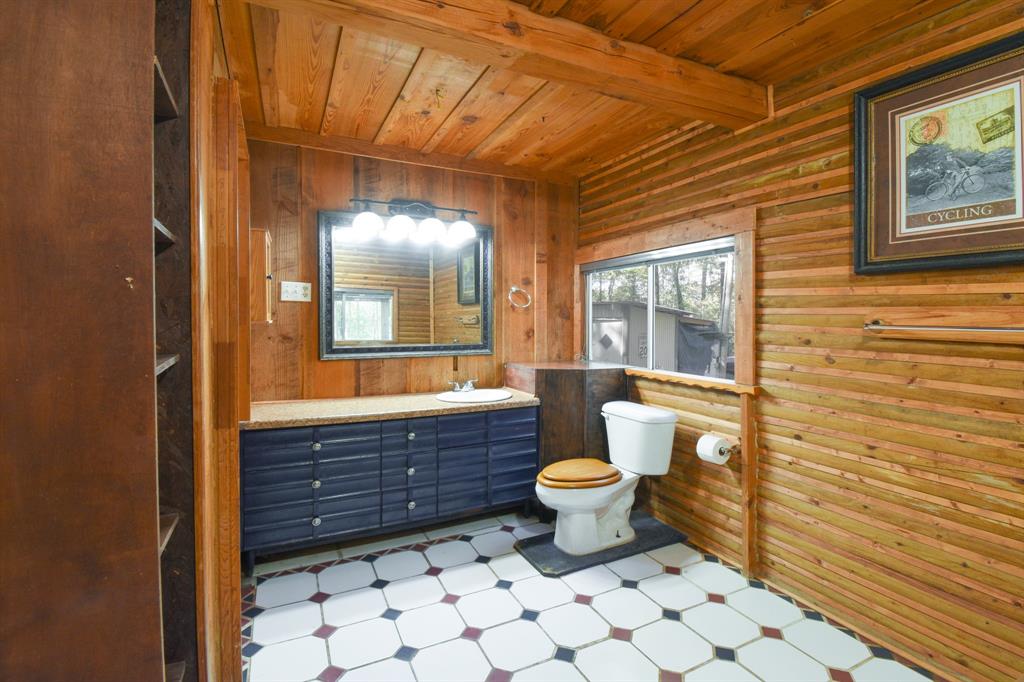 Large bathroom with wood ceiling and walls, tile floor, large vanity with decorative mirror, medicine cabinet and storage shelves.